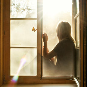 woman looking out of window with light and butterfly