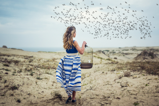 woman letting birds go from a cage, on sand