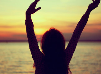 woman raising arms up sunset