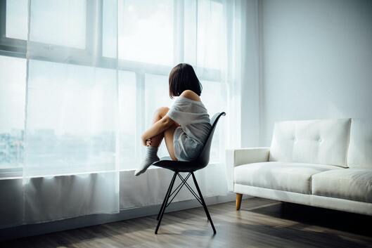 sad woman sitting on chair looking at closed curtains