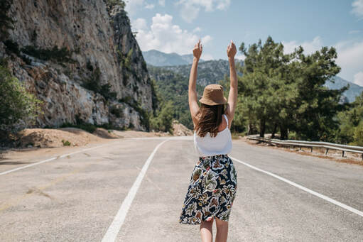 woman walking along road in mountainside, arms in air feeling free