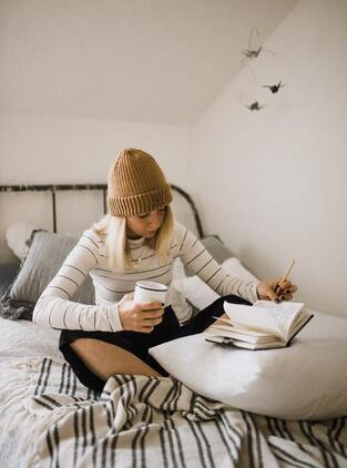 woman relaxing on bed with coffee mug and journal