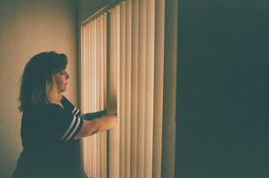woman in dark room looking out of curtains