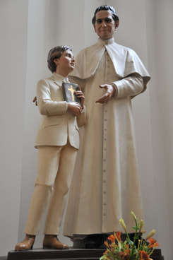 priest with arm around altar boy in white sculpture