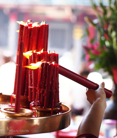 hand lighting long thin red candles in sacred place
