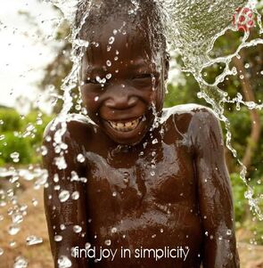 joy is in simplicity quote of happy child sprinkled by water