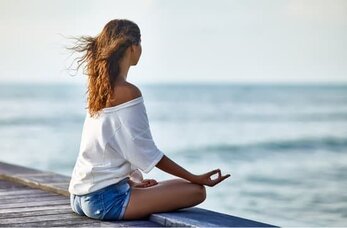 spiritual woman meditating on dock near sea