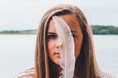 woman holding large white feather in front of face
