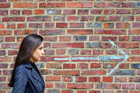 woman in front of brick wall with arrow pointing forward