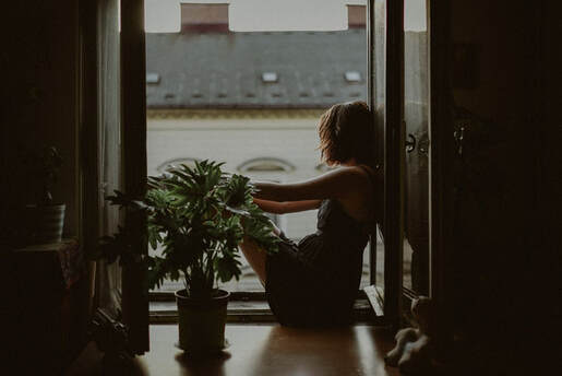 woman sitting by window in dark room feeling down