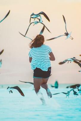woman running on beach with seagulls