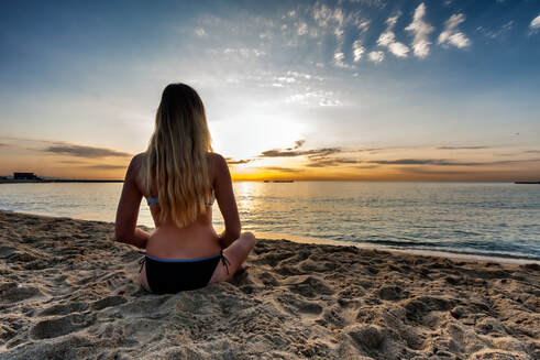 woman meditating on beach at sunset